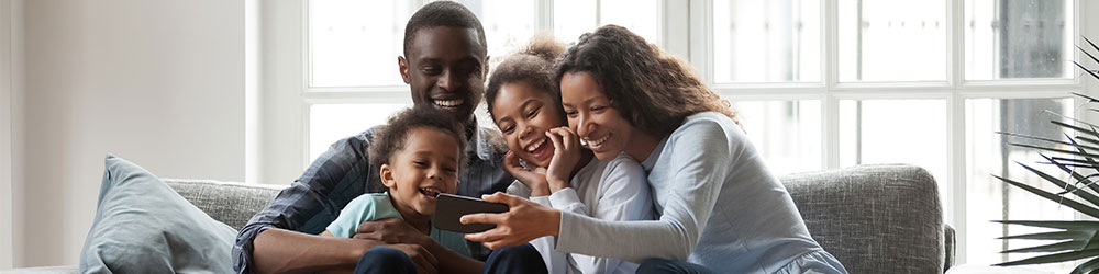 family on couch laughing and looking at mobile device